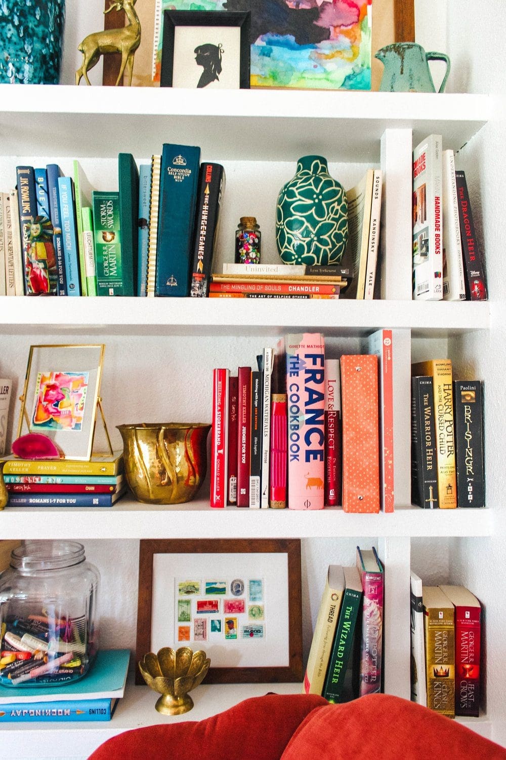 A cozy interior scene featuring a green armchair, a bookshelf filled with books, and a yellow articulated lamp. A small wooden table with books and a houseplant sits next to the chair. The room has warm lighting and a relaxed atmosphere.