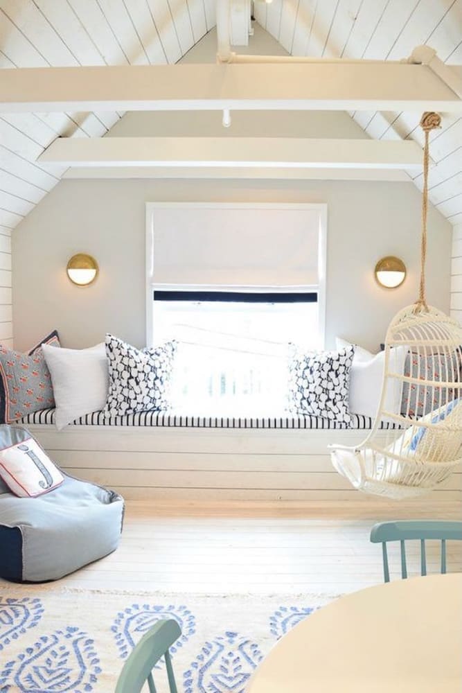 Light-filled vacation home interior design featuring a cozy loft nook with a built-in window seat, graphic pillows, and a rattan swing chair—designed for both play and relaxation in a family-friendly retreat.
