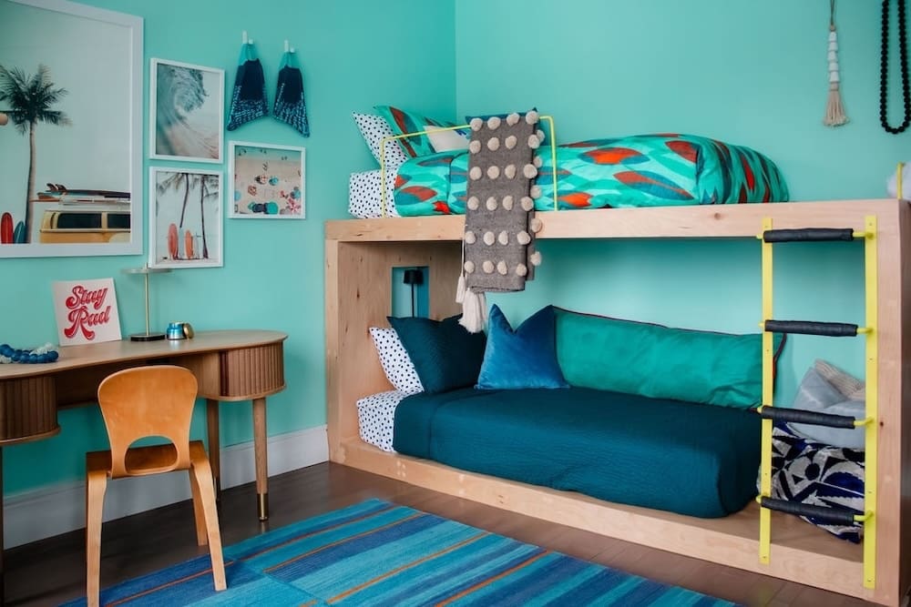 Custom-designed elevated escape interior by Indigo Ink Interiors featuring a surf-themed kids' bedroom with built-in bunk beds, tropical turquoise walls, and playful, layered textiles. A bold and personal take on vacation home interior design with modern maximalist flair.