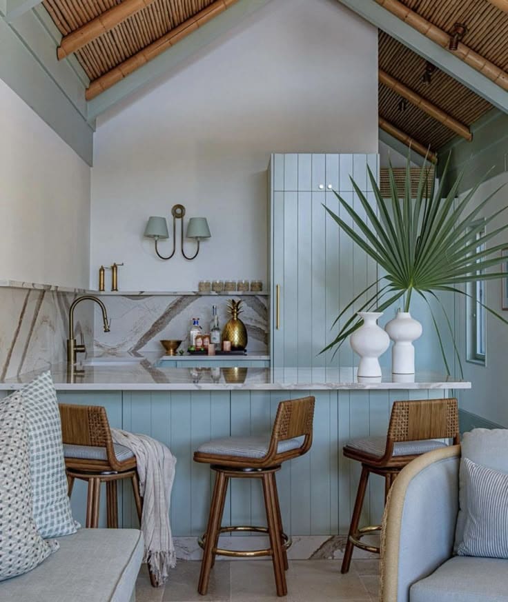 Vacation home interior design featuring a coastal-inspired kitchen with pale blue cabinetry, bamboo ceiling, rattan bar stools, and a bold marble backsplash—perfectly blending laid-back elegance and function.